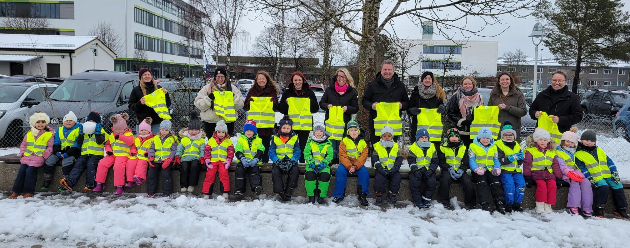 Kinder aus dem Kindergarten Villa Kunterbunt mit Warnwesten gekleidet. Dahinter stehen Erzieherinnen und Stadtwerke Mitarbeiter mit Warnwesten in der Hand.